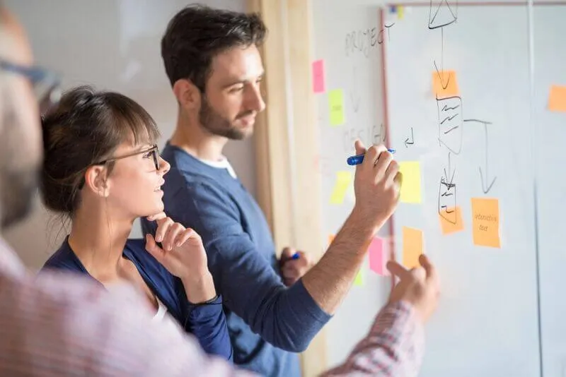 People are writing on a board, which is covered with sticky notes