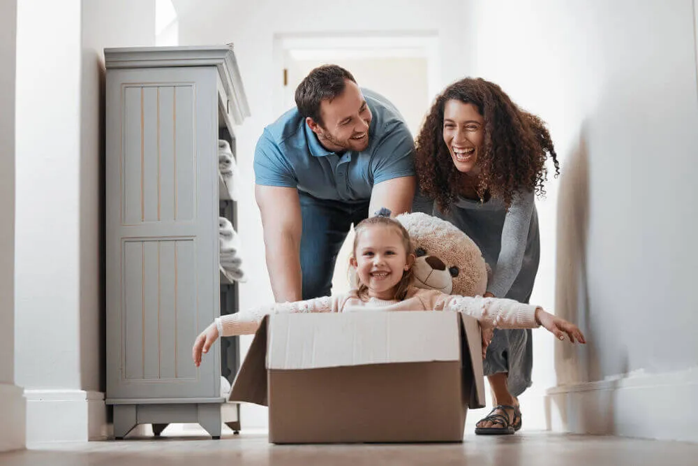 Mother and father playfully pushing a box with their child in along the floor