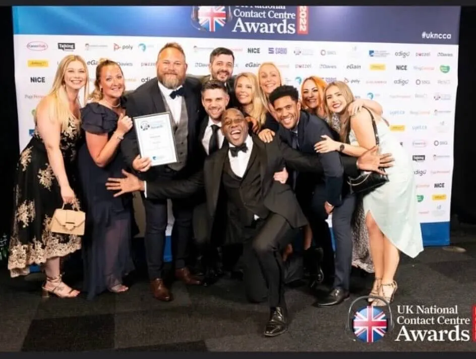 The Atom bank Contact centre team holding an award they won at the UK National Contact Centre awards with Ainsley Harriott crouching and smiling in front of them