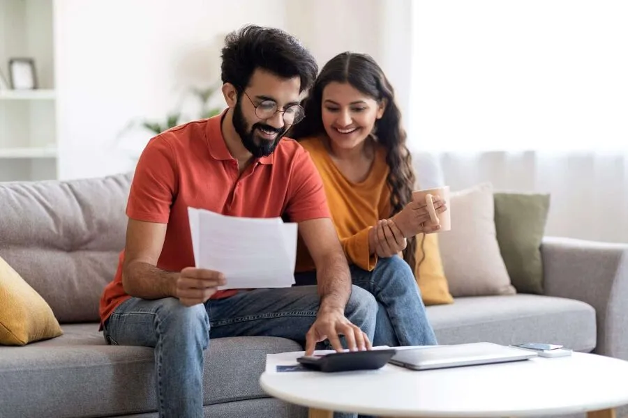 A couple sitting on the couch and looking at some papers while smiling.