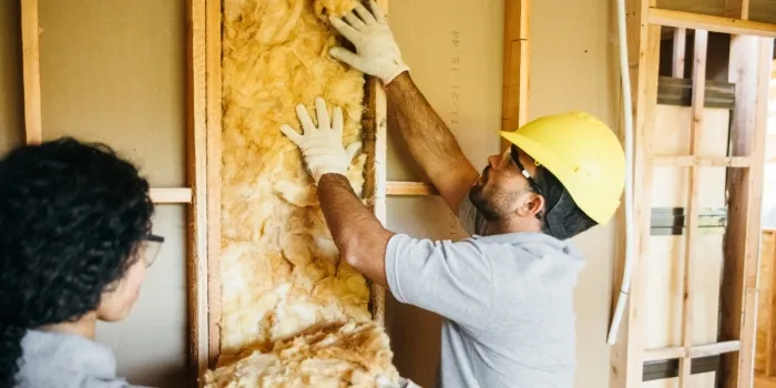 A person wearing a hard hat presses insultation material into a structure