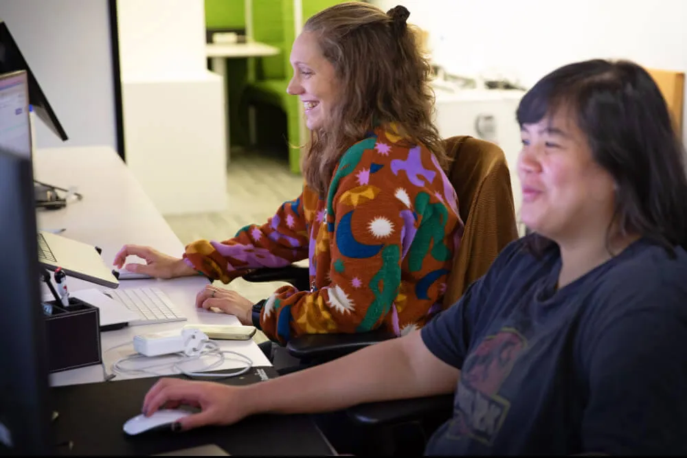 Two people laughing as they are working at their desks on computers