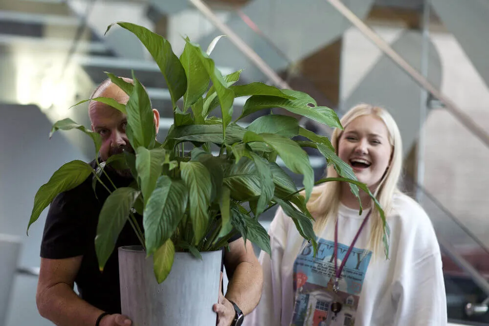 Man holding a plant with a woman behind laughing