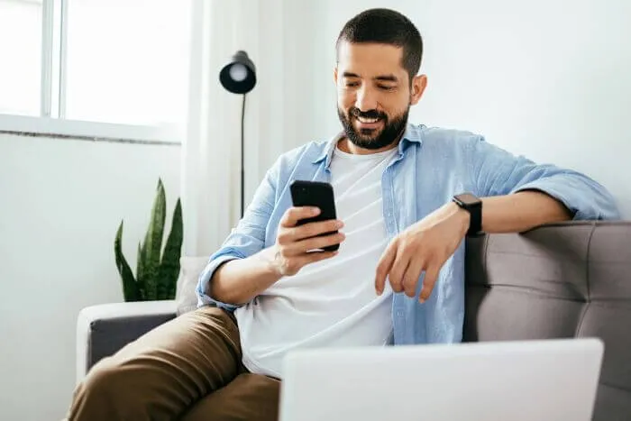 Person sitting on sofa looks at their phone and smiles