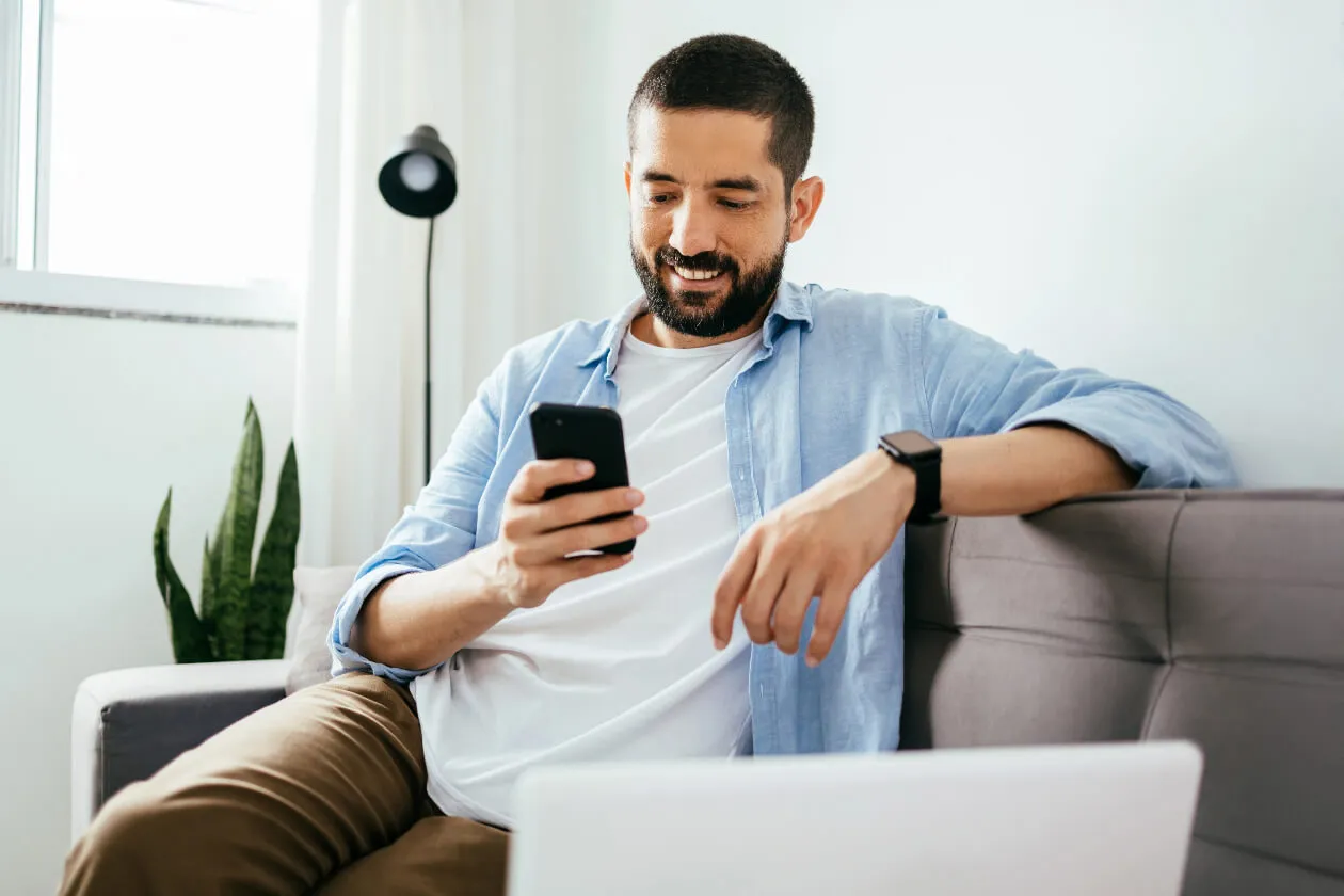 Person sitting on sofa looks at their phone and smile