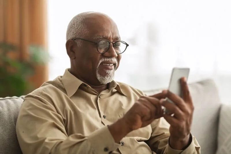 A person wearing a shirt and glasses interacts with their phone, looking happy