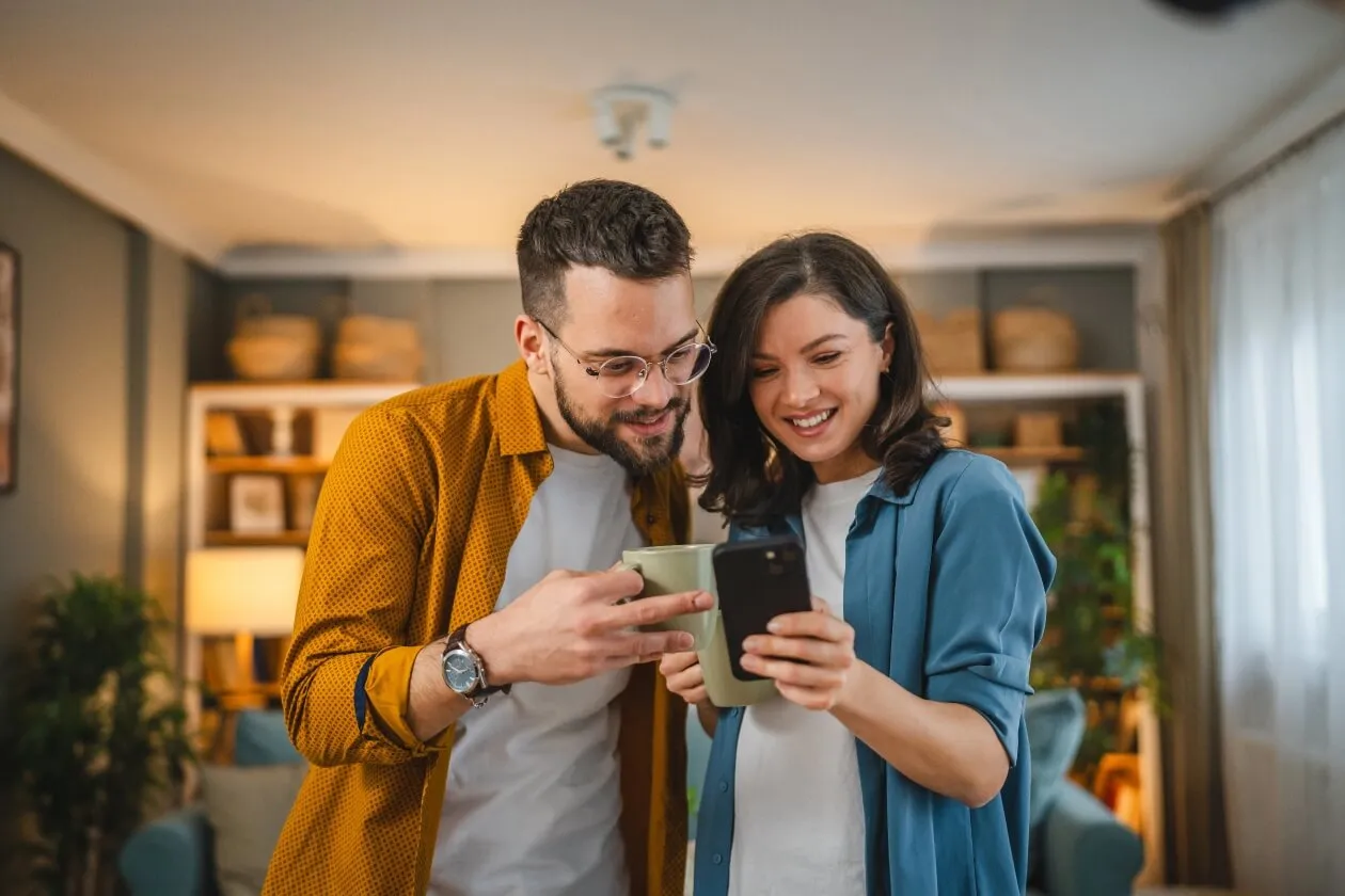 Two smiling people hold mugs and observe smartphone screen