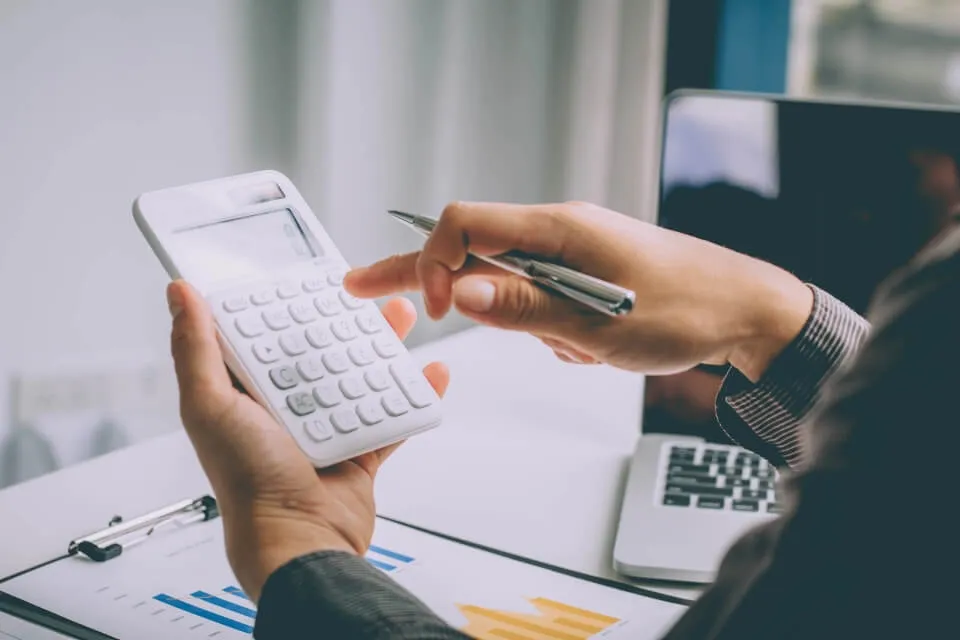 Person types into a calculator with a pen in their hand