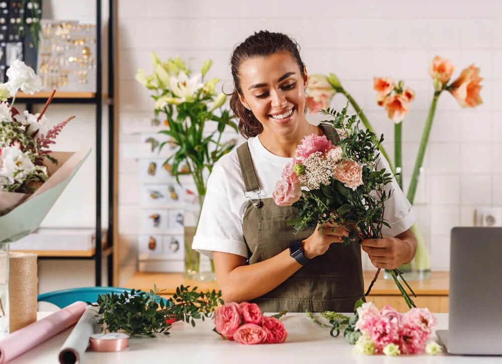 A woman is standing by a desk preparing some flowers