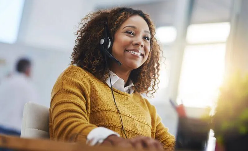 Someone in a yellow jumper, wearing a headset, smiles